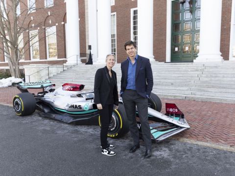 Toto Wolff stands confidently beside a Mercedes Formula One car outside an academic building, symbolizing high-performance leadership and the mindset behind championship-level success.