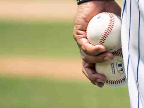 Close-up of a baseball player holding two baseballs on a field, symbolizing strategy and execution in sales leadership.