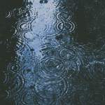 F1 race car driving through heavy rain spray creating massive water plumes, demonstrating wet weather racing challenges and the leadership skills required to excel in uncertainty