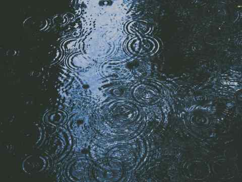 F1 race car driving through heavy rain spray creating massive water plumes, demonstrating wet weather racing challenges and the leadership skills required to excel in uncertainty